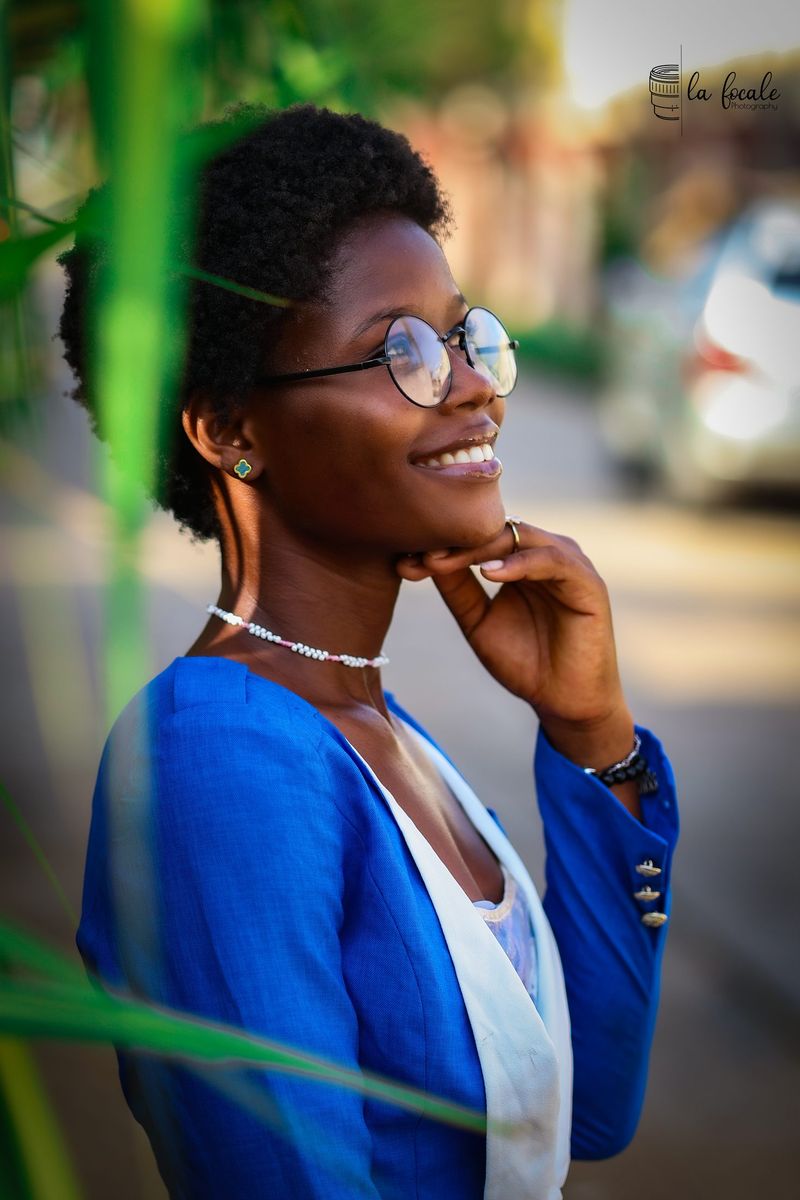 Profile portrait of a smiling young woman in round glasses and a blue blazer, hand to chin