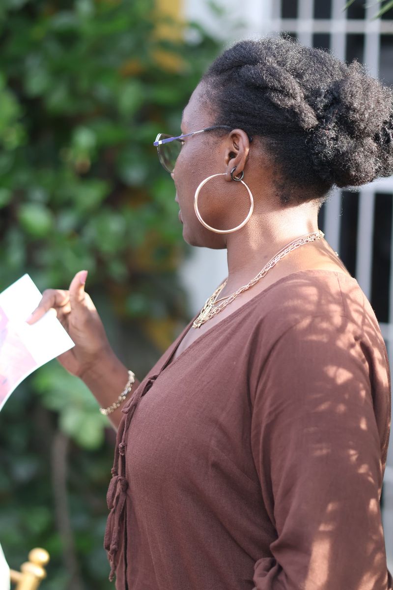A woman in brown with hoop earrings speaks while holding a sheet of paper