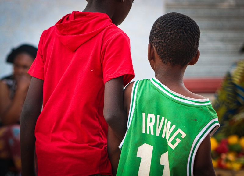 Two boys seen from behind, one in a red hoodie and one in a green basketball jersey reading Irving