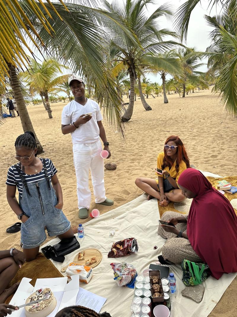 A group of friends gather on a picnic blanket under palm trees at the beach book club