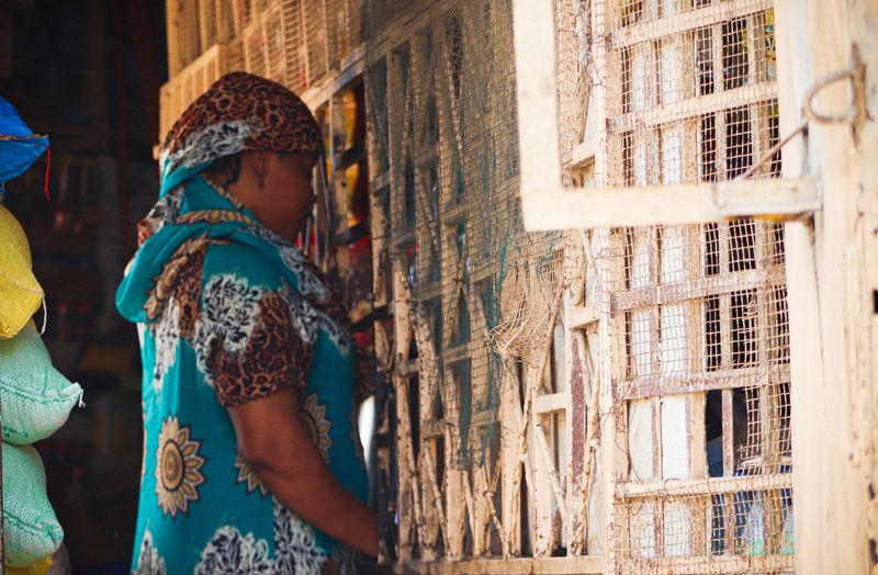 A woman in a turquoise patterned dress browses woven baskets at a market stall