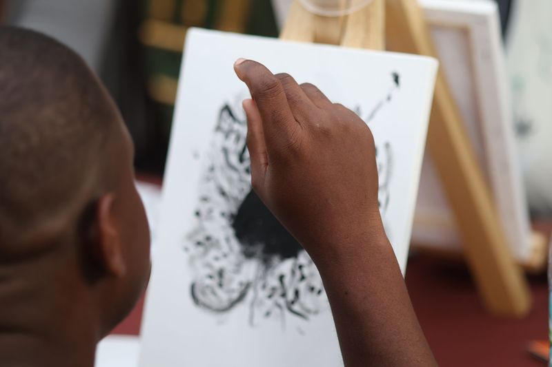 A guest paints a black abstract design on a canvas at the painting workshop
