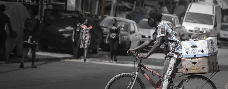 A young man cycles through city traffic carrying a box on his bicycle