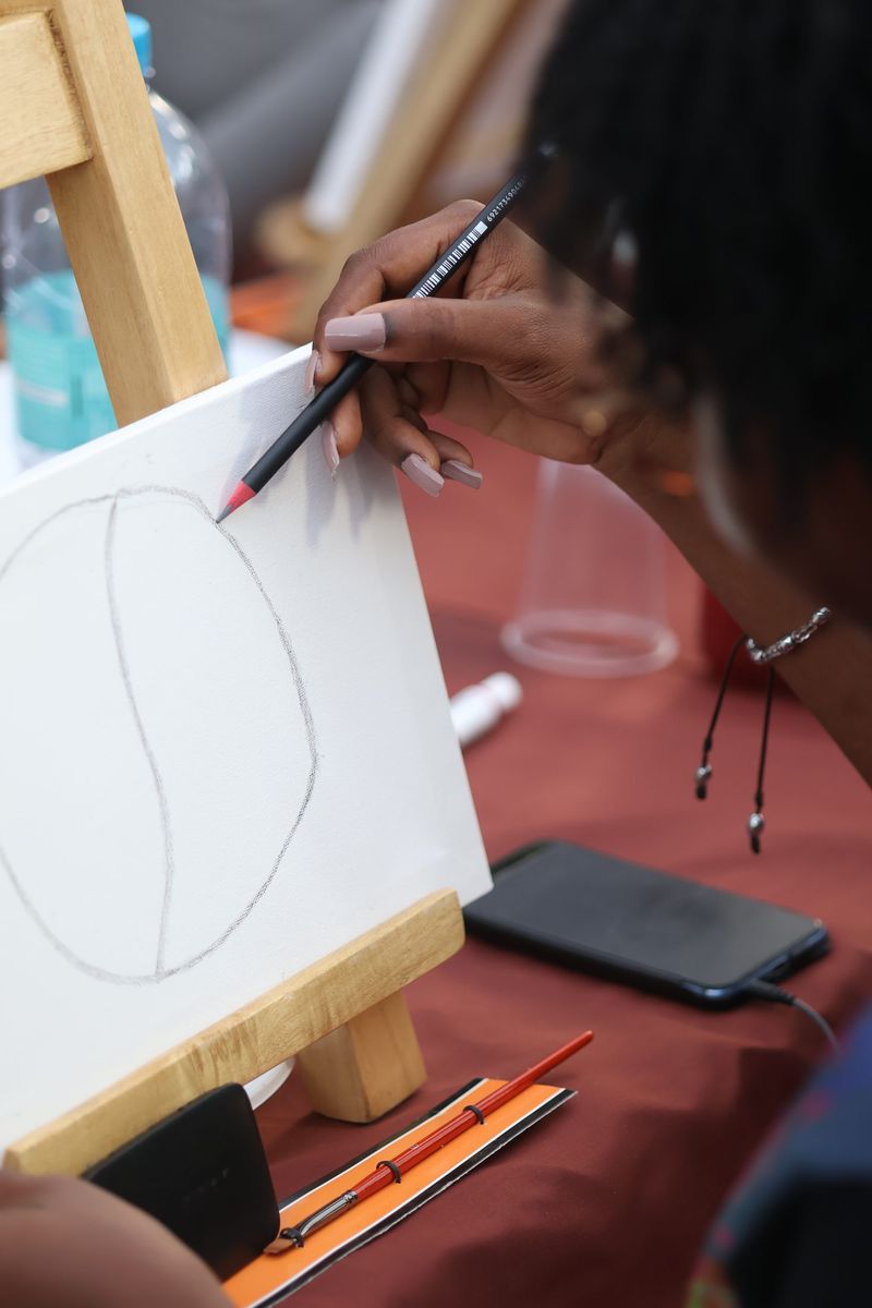 A hand outlines a shape on a canvas with a brush at the painting workshop