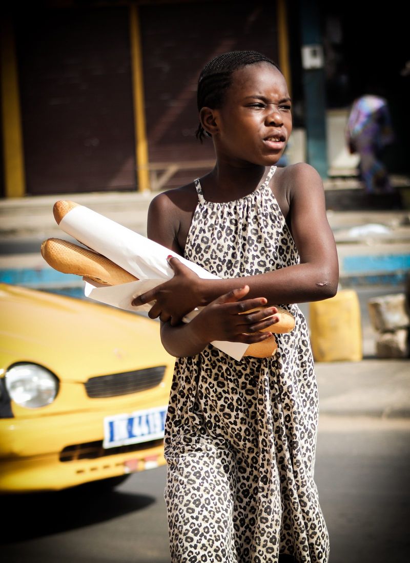 A girl in a leopard-print dress carries baguettes past a yellow taxi on the street