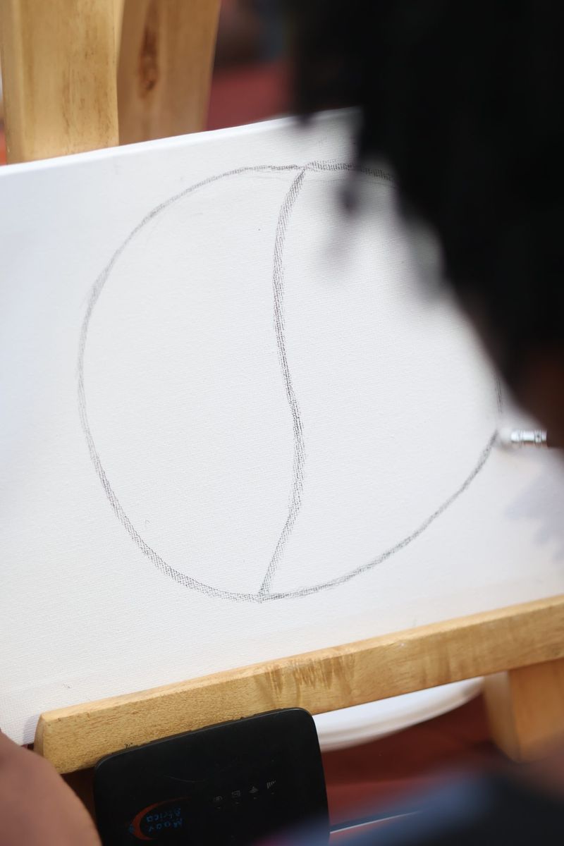A canvas on an easel shows a sketched outline as a guest works behind it