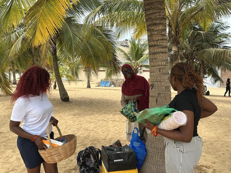 Friends set up a beach picnic under palm trees, one carrying a woven basket