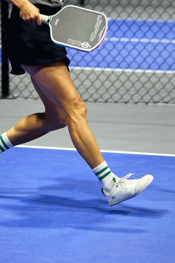 Close-up of pickleball player flexing calf muscle, wearing Atomic Court, Classic Court (white, green) colorway.