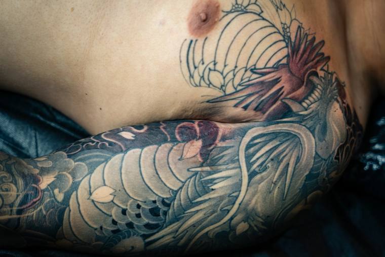 Large Japanese irezumi tattoo of a red and grey dragon with wind bars and clouds wrapping around a man's side torso and ribs.