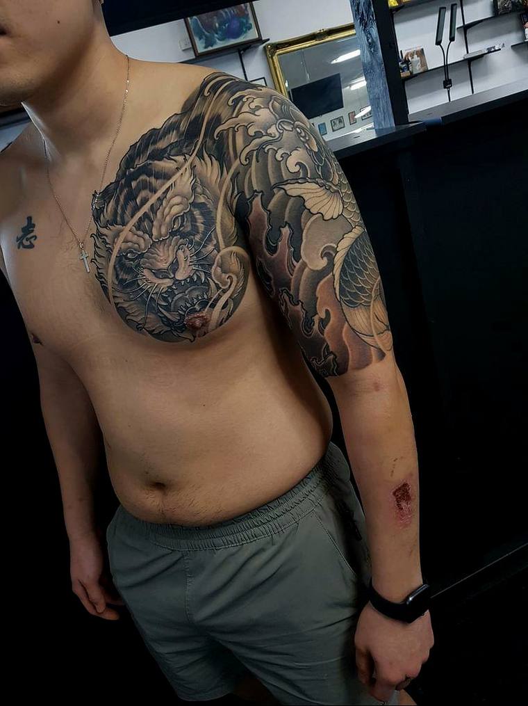 Man displaying a freshly completed irezumi tiger and koi tattoo across his right shoulder and upper arm, with visible irritat