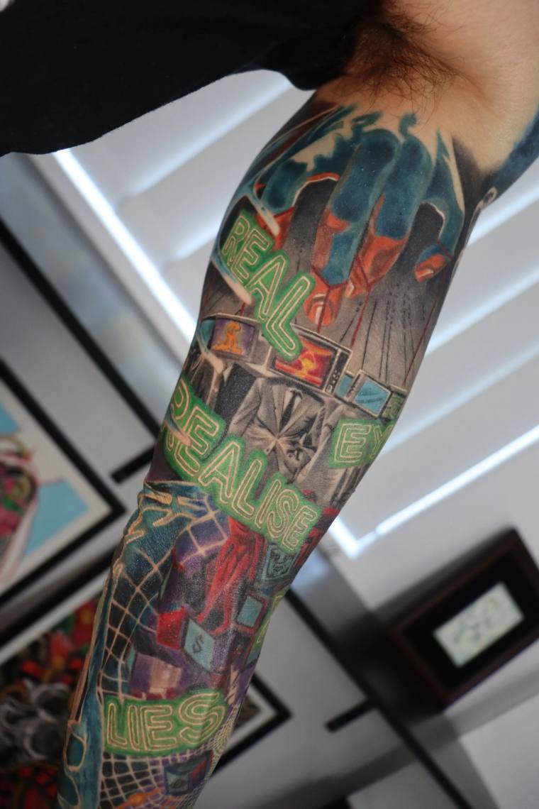 Finished forearm sleeve tattoo featuring neon-style lettering reading 'REAL', 'REALISE', and 'LIES' in green, red, and black
