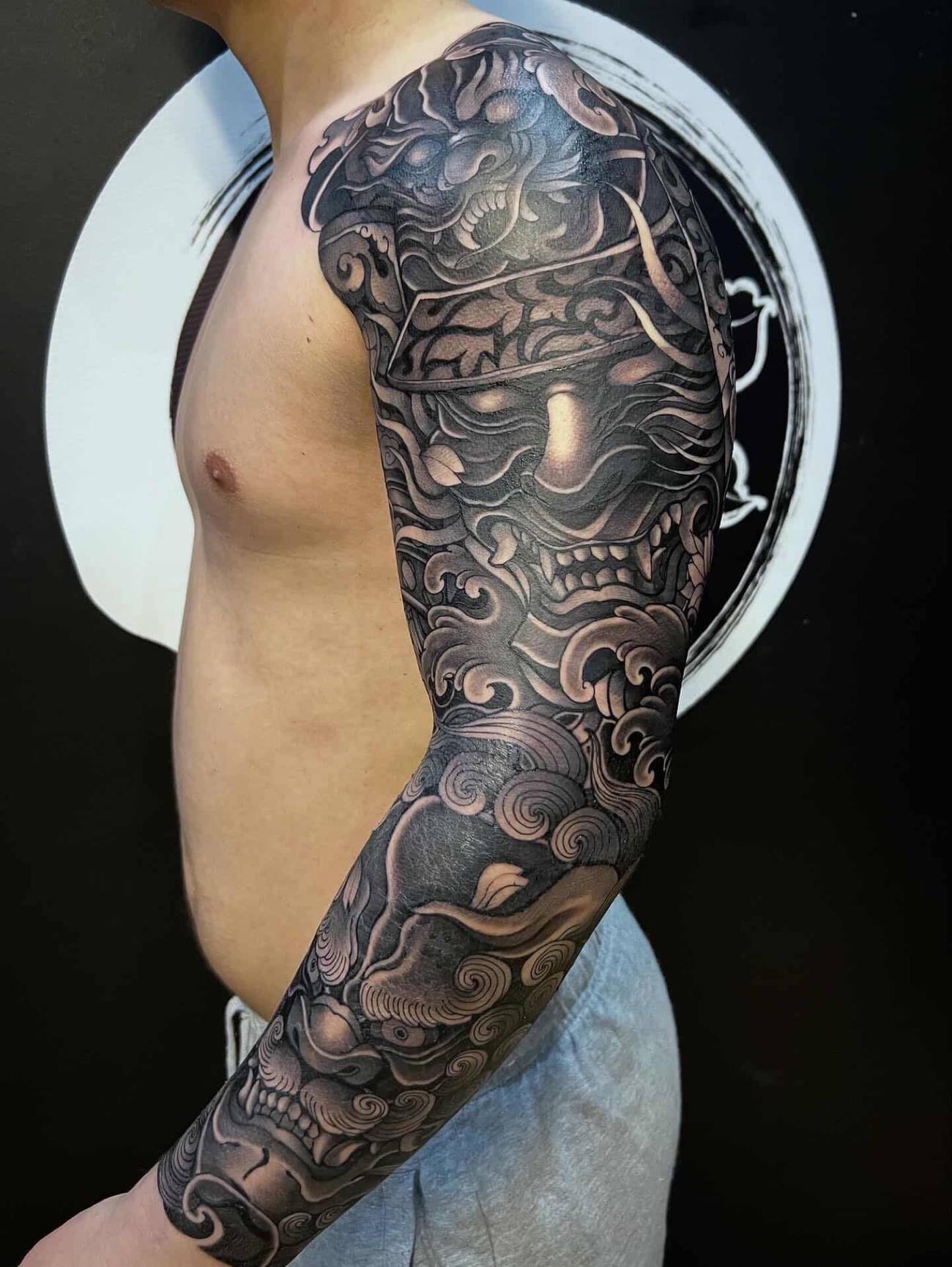 Phil - A striking greywash irezumi full sleeve with stacked hannya and oni masks woven through traditional wind bars and cloud swirls.