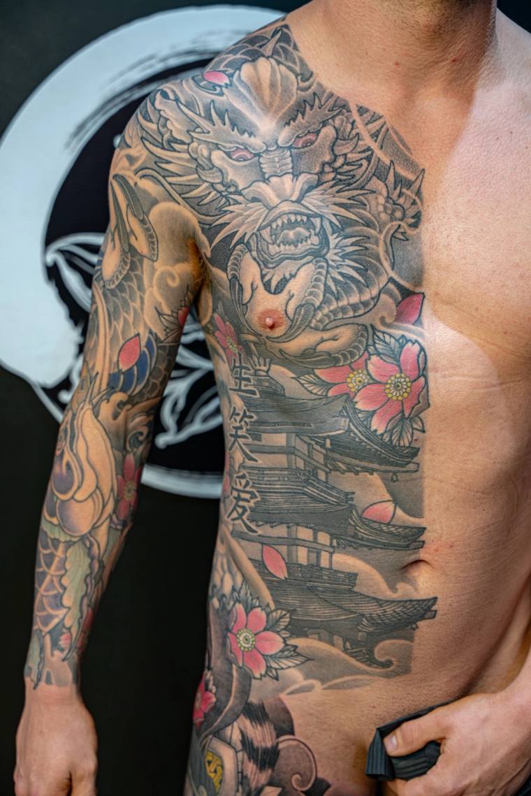 Finished irezumi half-sleeve and chest piece featuring a snarling dragon, cherry blossoms, a pagoda, kanji, and clouds in bla