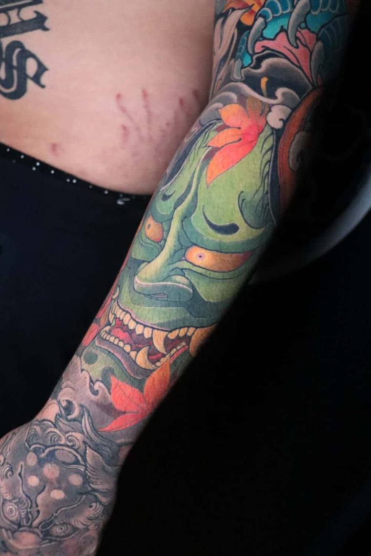 Vibrant Japanese irezumi full sleeve featuring a green oni demon mask, orange maple leaves, and koi with waves.