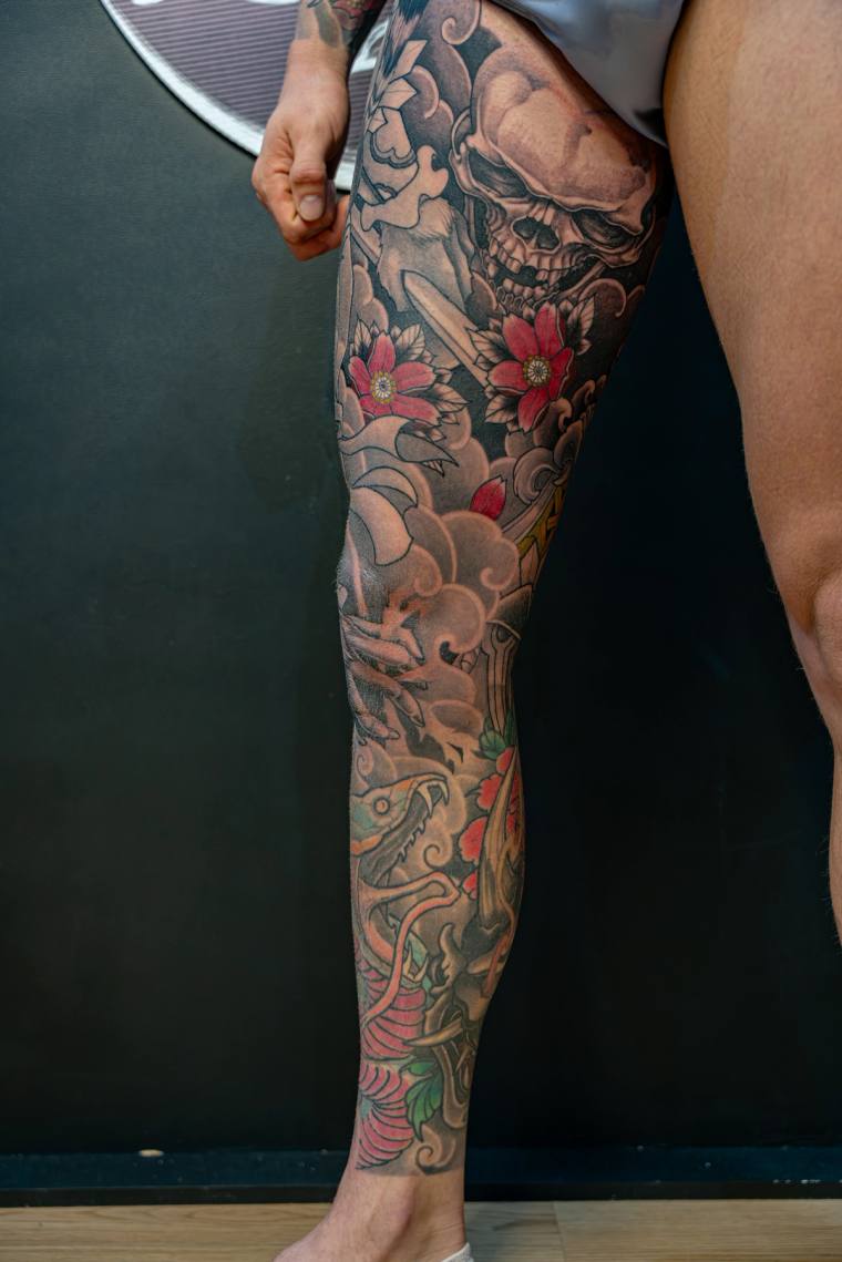 Finished irezumi full-leg sleeve featuring a skull, red cherry blossoms, clouds, a coiling snake, and a koi fish near the ank