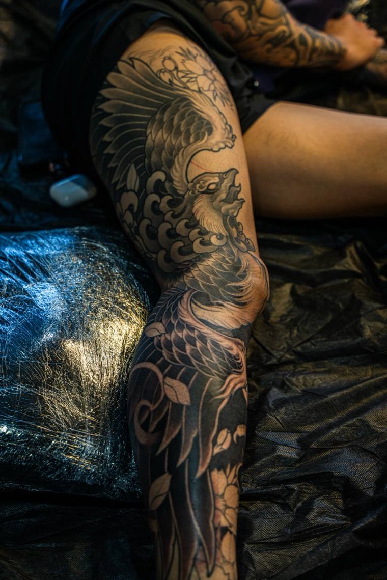 Large Japanese-style phoenix leg sleeve tattoo in blackwork, featuring detailed feathers, swirling clouds, and floral accents