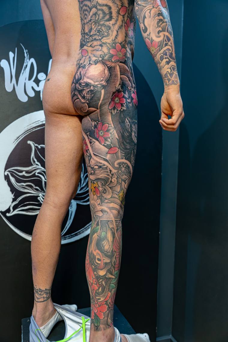 Finished Japanese irezumi leg sleeve featuring a daruma doll, cherry blossoms, skull, hannya mask, and wave patterns in red, 