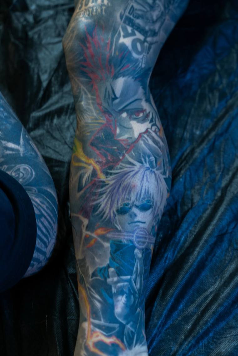 Finished color anime-style tattoo on a forearm featuring Soul Eater character portraits with red and yellow lightning effects