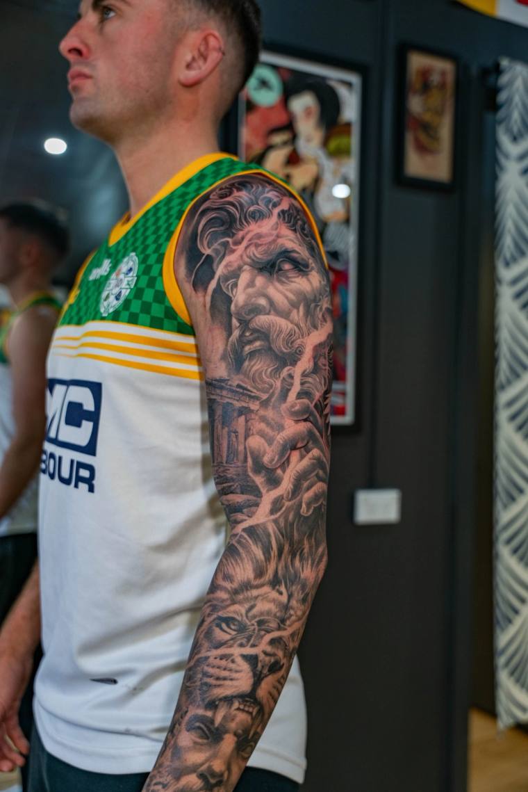 Finished greywash full sleeve on a man wearing a green and white sports jersey, featuring a bearded deity, tiger, and mytholo