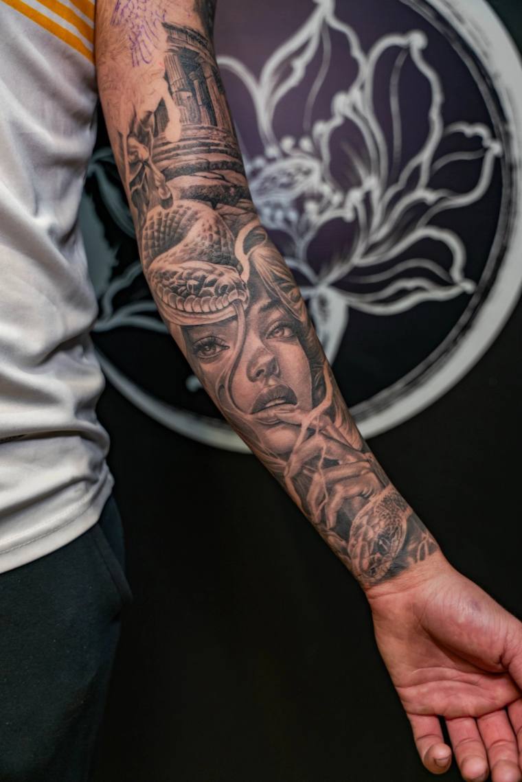 Finished black and grey forearm sleeve tattoo featuring a woman's face with a coiled snake, a koi fish at the wrist, and temp