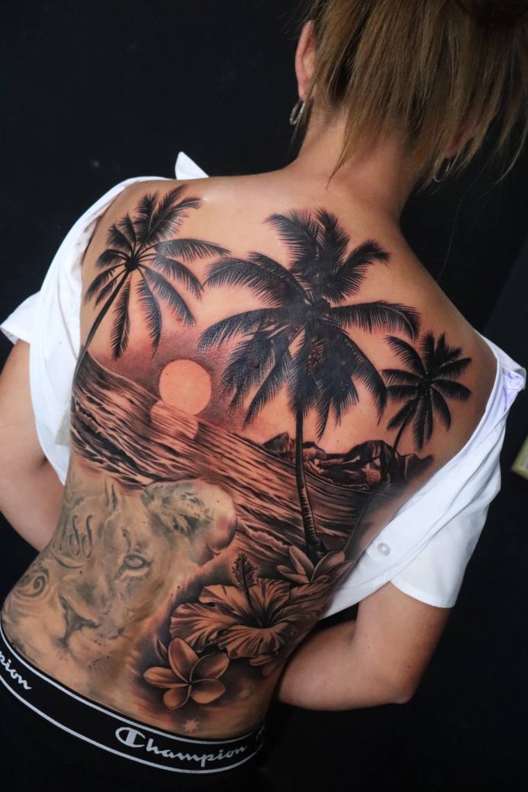 Large black and grey back tattoo featuring palm tree silhouettes, a sunset over ocean waves, a tiger's face, plumeria flowers