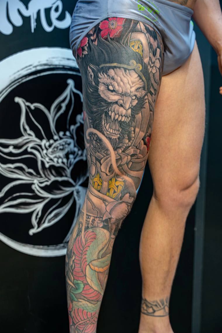 Colorful Japanese irezumi thigh tattoo featuring a fierce hannya demon mask, coiled snake, chrysanthemum blooms, gold kanji c