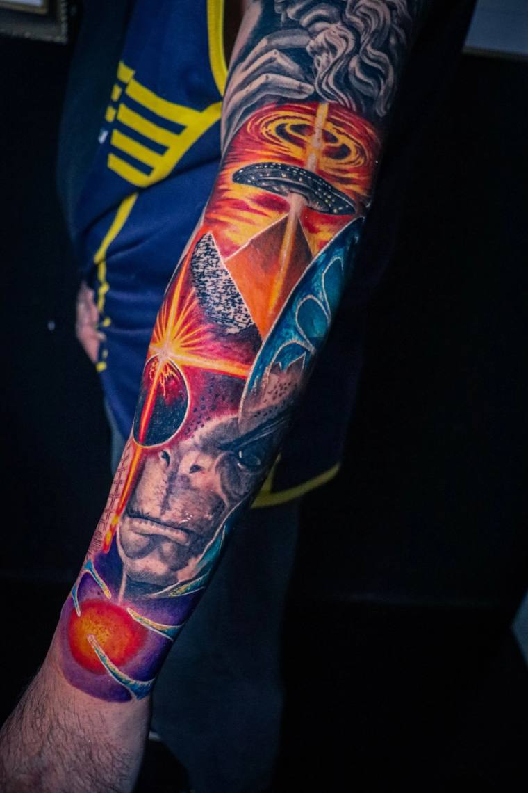 Colorful full-sleeve forearm tattoo featuring a detailed portrait of Thanos with a cosmic sword, swirling galaxy background, 