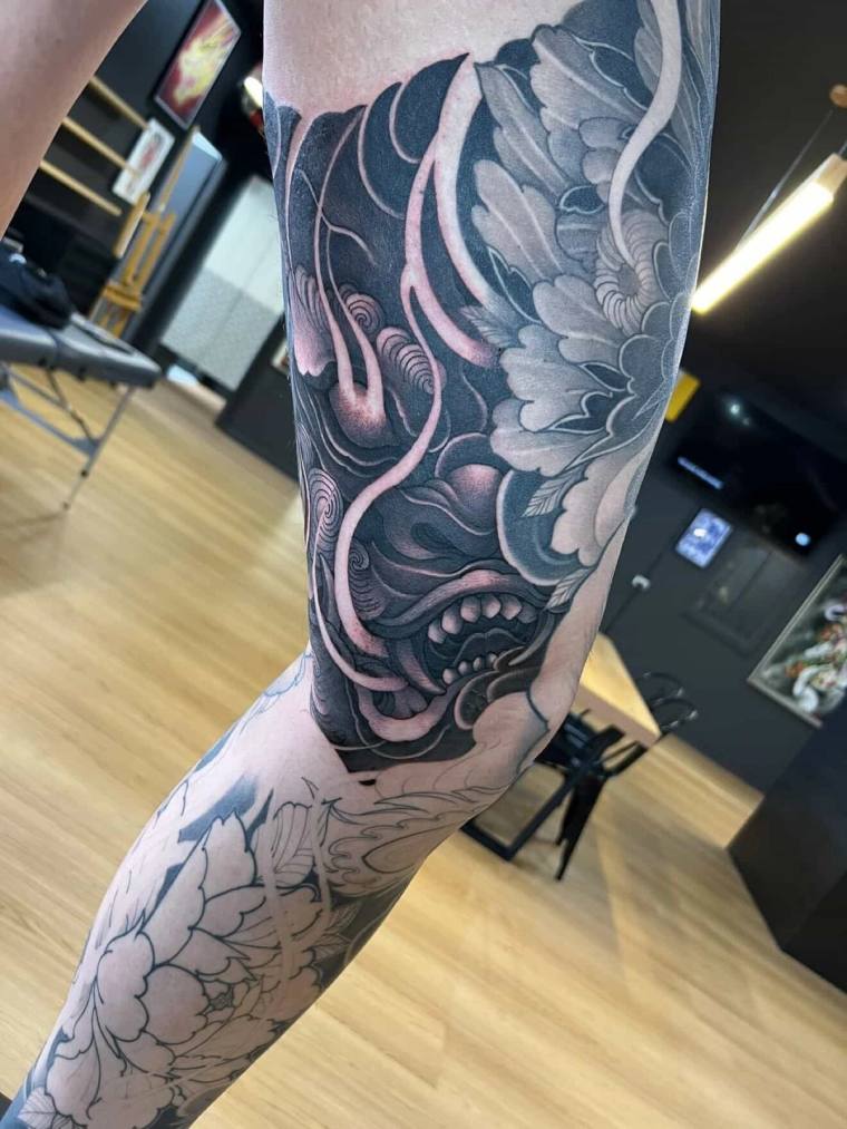 Finished blackwork irezumi forearm tattoo featuring a snarling Hannya demon mask surrounded by peony blooms and flame motifs.