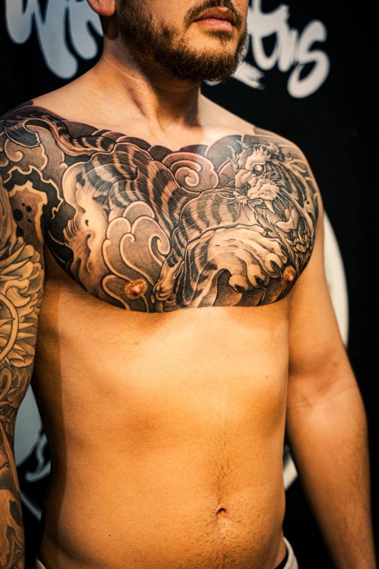 Finished black and grey irezumi chest tattoo of a snarling tiger with extended claws, framed by traditional wind bars and clo
