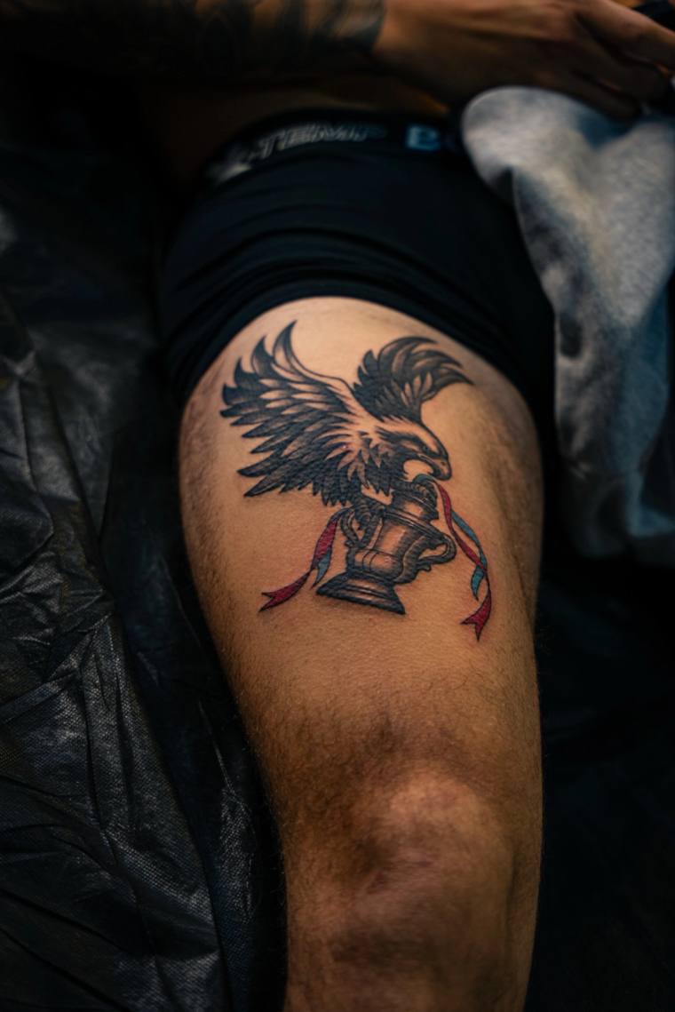Neo-traditional eagle tattoo clutching a chess rook with flowing red and blue ribbons on a thigh.
