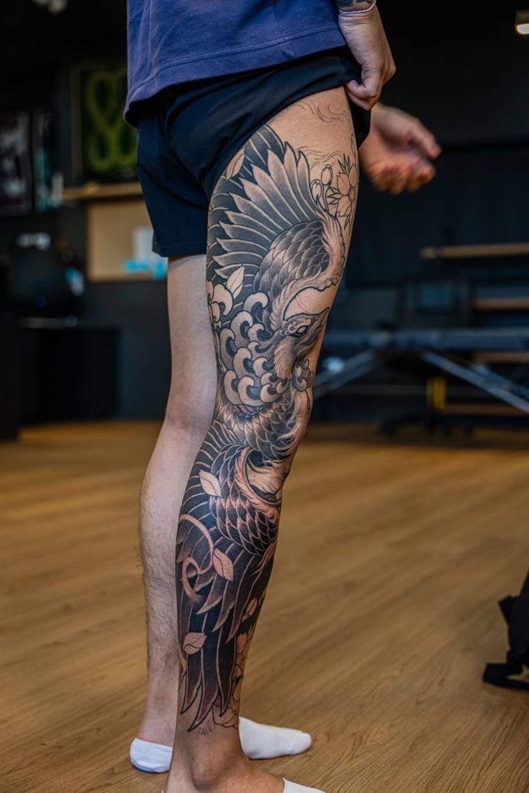 Japanese irezumi full leg sleeve featuring a crane in flight, cherry blossoms, and traditional wave motifs in black and grey.