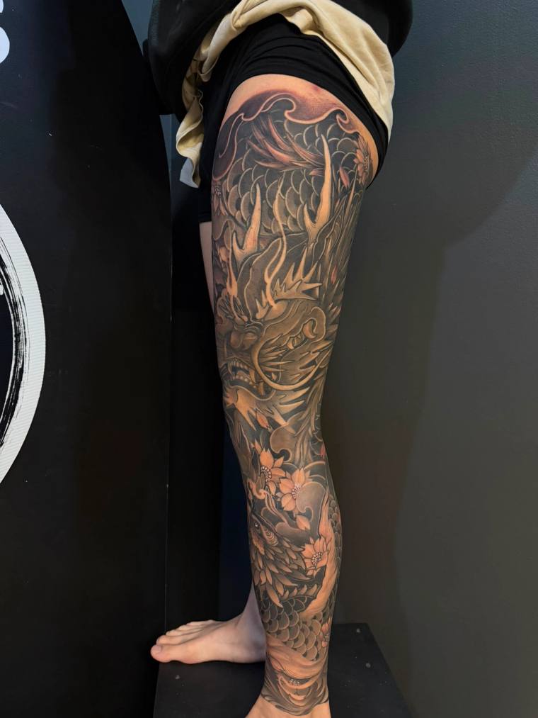 Black and grey full leg sleeve with an aggressive dragon and a phoenix on the lower half.
