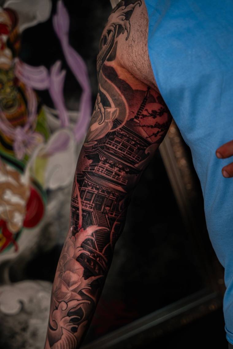 Finished Japanese-style sleeve tattoo featuring a multi-tiered pagoda and crashing waves, dramatically lit with red light on 