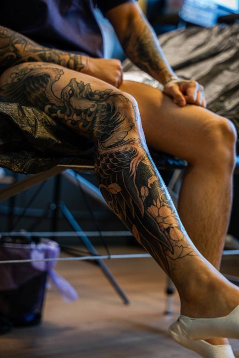 Finished irezumi leg sleeve featuring koi, ocean waves, and peony flowers in blackwork, photographed on a seated client.