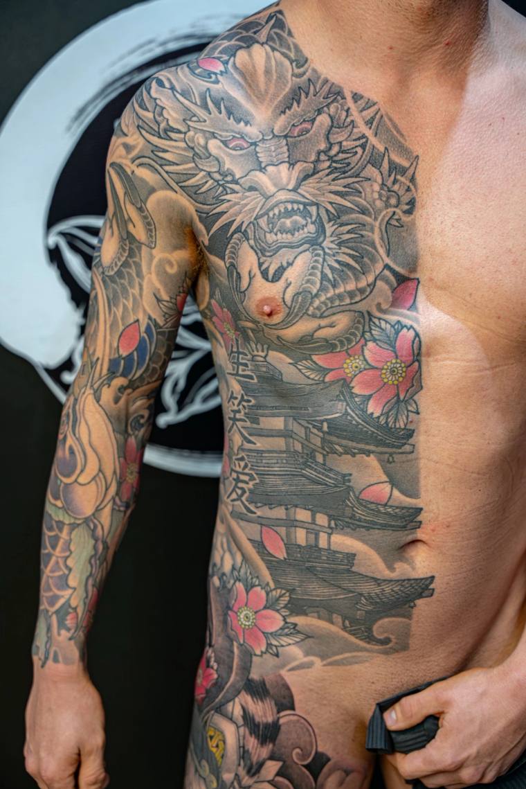 Healed irezumi half-sleeve and side chest piece featuring a snarling oni face, pagoda, pink cherry blossoms, and crashing wav