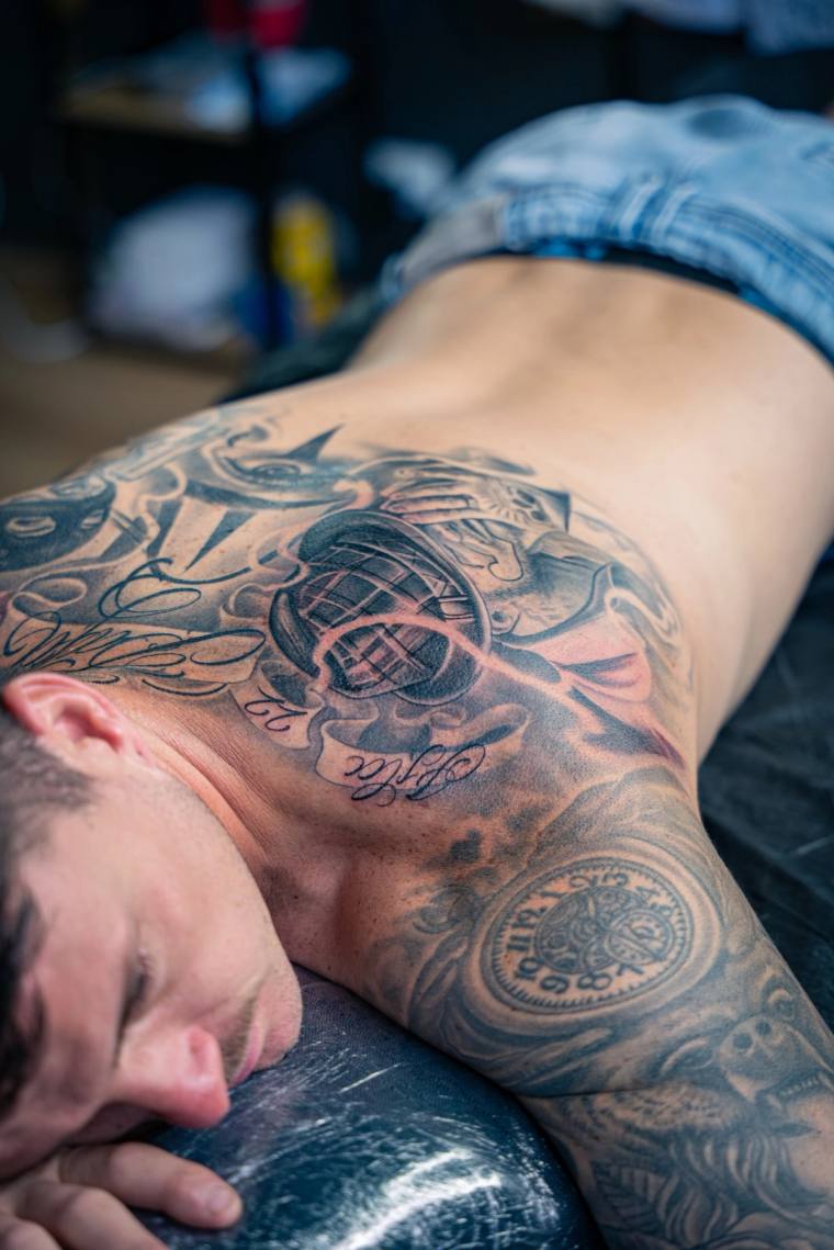 Man lying face down showcasing an intricate irezumi-style black and grey samurai tattoo covering his back, neck and shoulder.