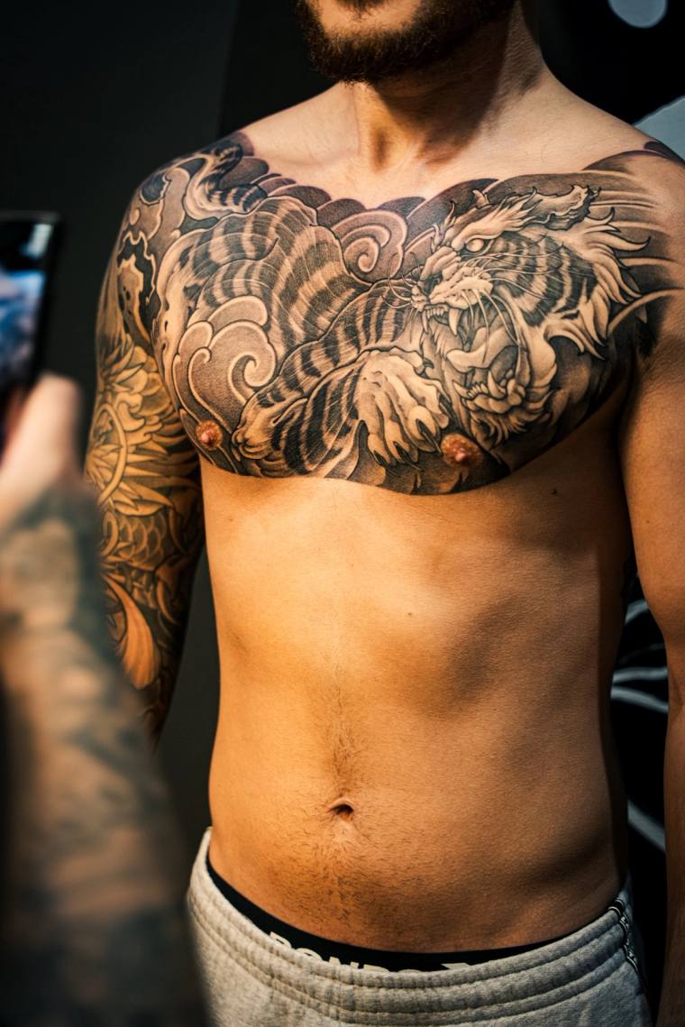 Healed irezumi chest tattoo of a roaring tiger amid swirling waves and clouds on a man's torso, with matching sleeve visible.