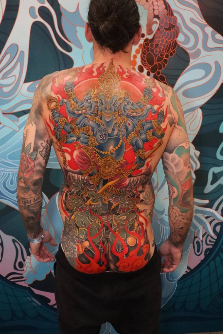 Full back and sleeve irezumi tattoo featuring a multi-armed elephant-headed deity surrounded by flames above demons, with flo