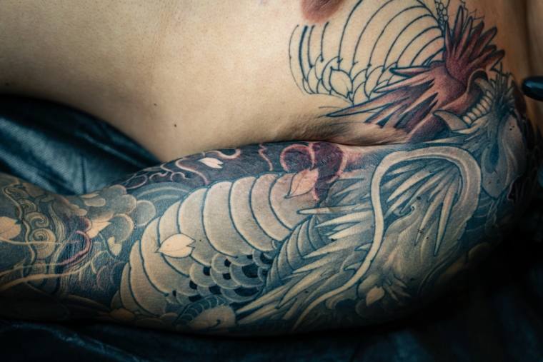 Japanese irezumi sleeve tattoo featuring a detailed koi fish with scales and a dragon head, wrapped around the forearm.