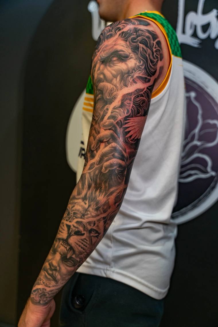 Side view of a man in a white tank top showing off a finished black and grey irezumi sleeve featuring a serene face and a fie