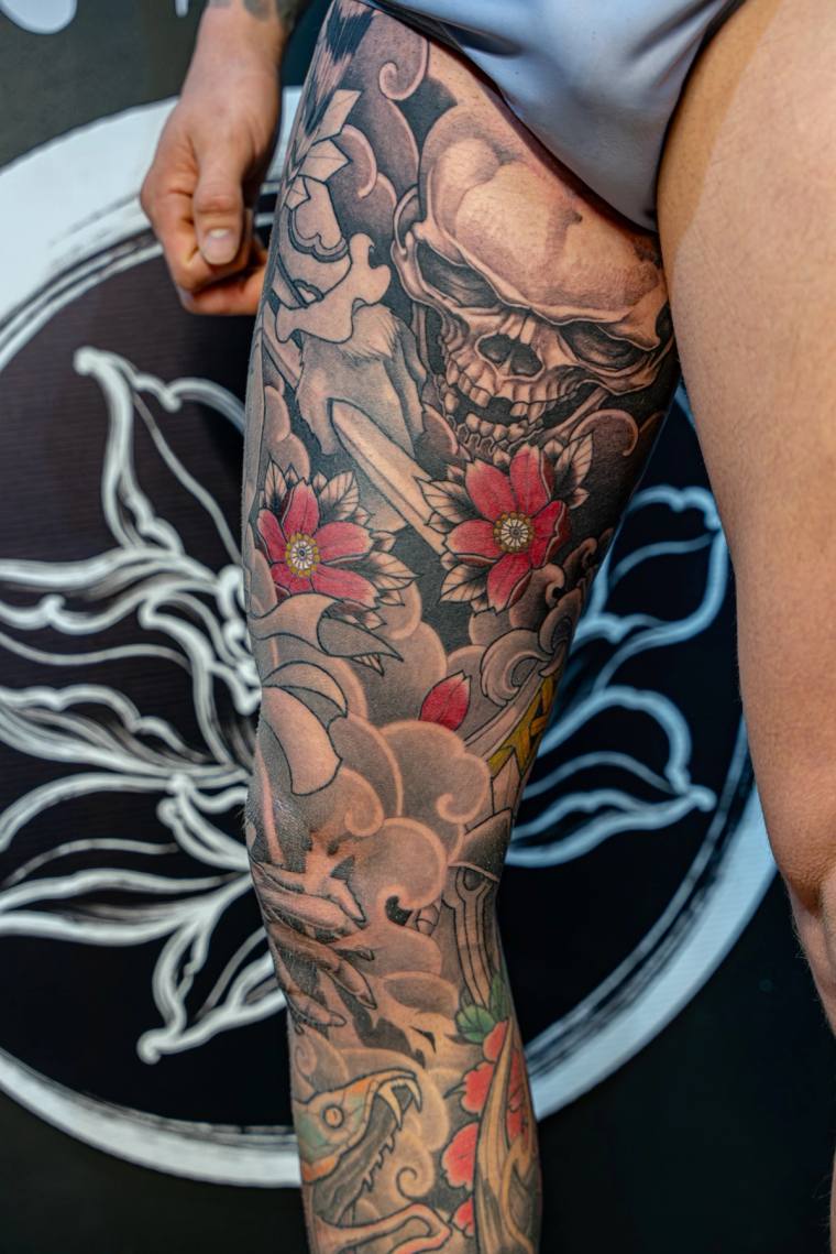 Finished irezumi leg sleeve featuring a demon skull, red blossoms, koi fish, crane, and traditional Japanese wind bars and cl