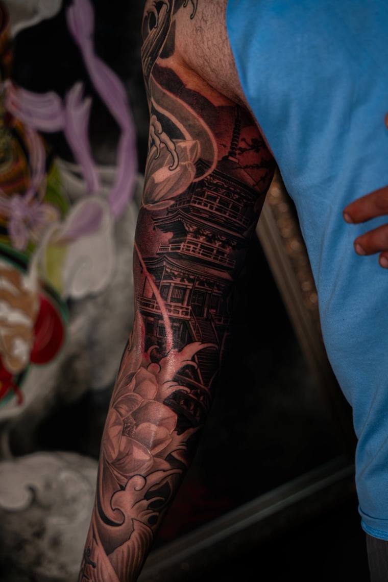 Japanese irezumi sleeve tattoo featuring a pagoda, koi fish, lotus flowers, and flowing water in black and grey with red acce