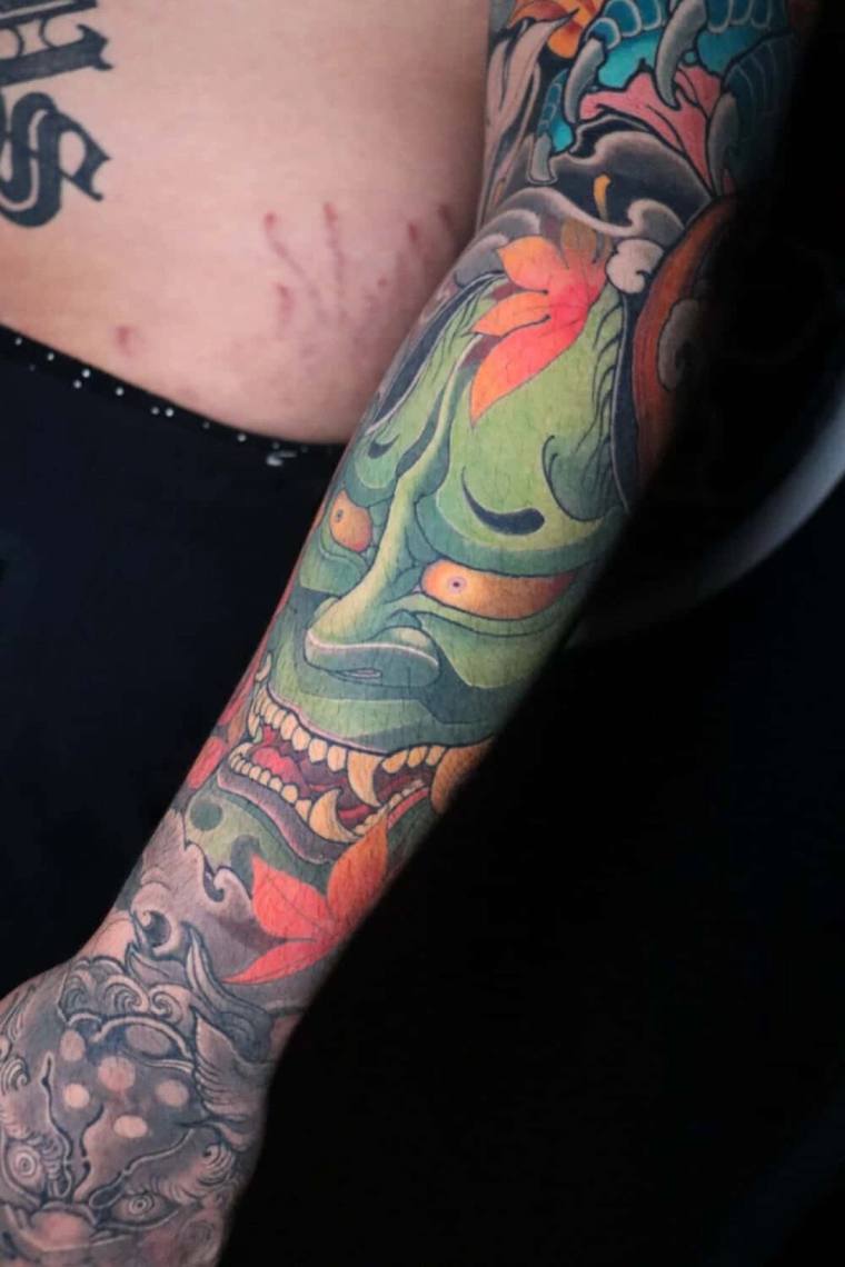 Vibrant Japanese irezumi full sleeve featuring a green oni demon mask, orange maple leaves, and koi with waves.