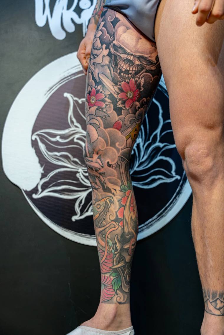 Japanese irezumi full leg sleeve featuring a samurai skull, katana, cherry blossoms, dragon, and wind bar clouds in colour an