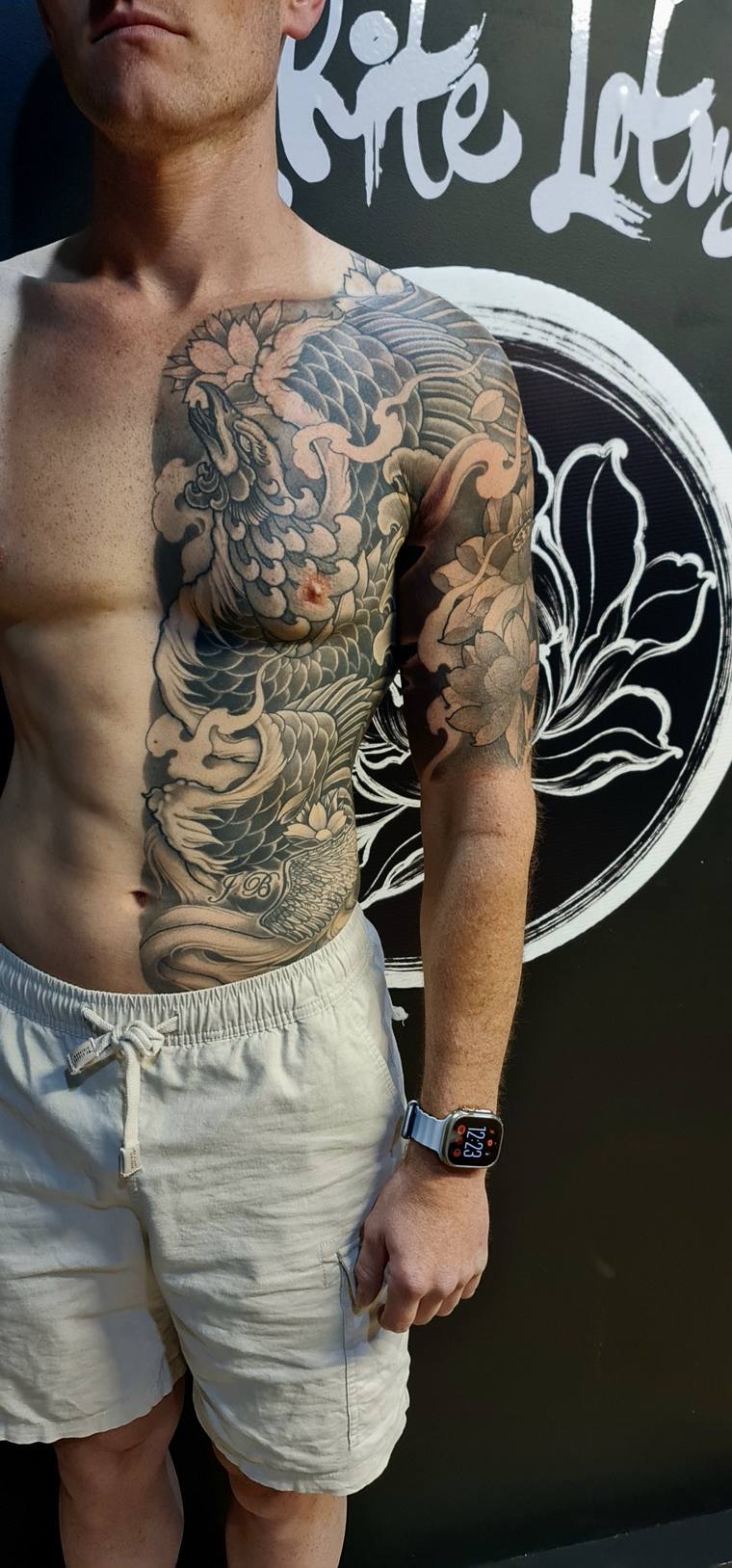 Finished irezumi half-sleeve tattoo on a man's left shoulder and arm featuring a koi fish, chrysanthemum, and waves in greywa