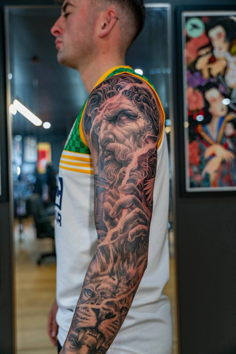 Black and grey Japanese-style full sleeve tattoo featuring a serene deity face with reaching hands on the upper arm and a sna