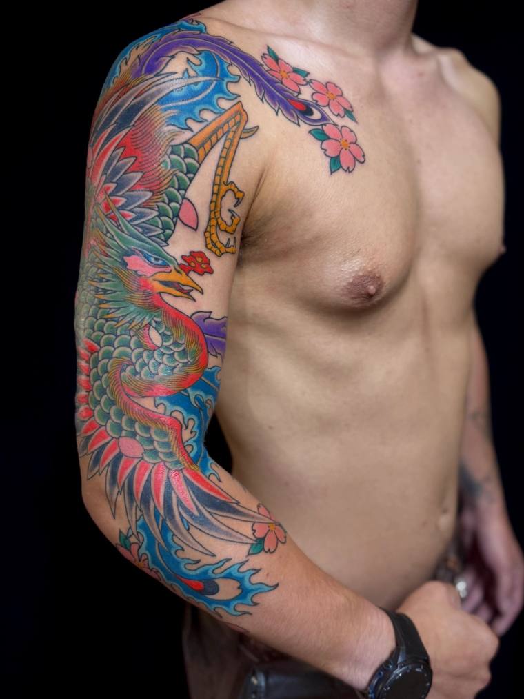 Finished Japanese irezumi half sleeve on a man's right arm featuring a colourful phoenix amid blue waves, pink cherry blossom