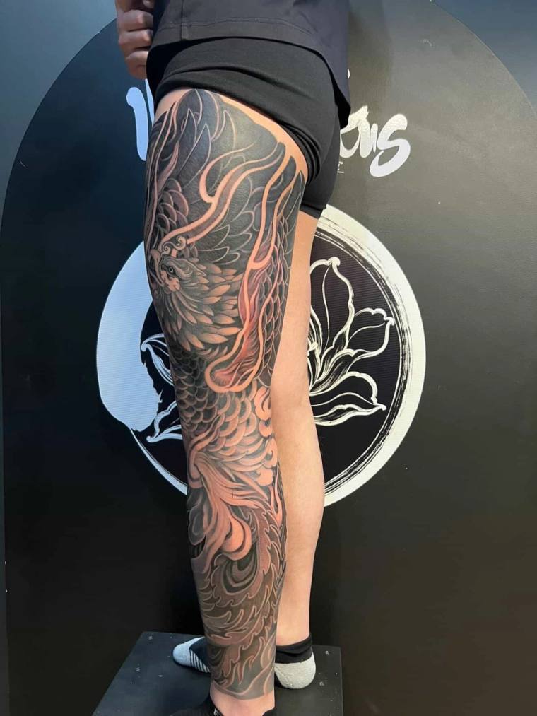 Large black and grey irezumi phoenix tattoo with flowing flames and detailed feather work on a person's outer calf.