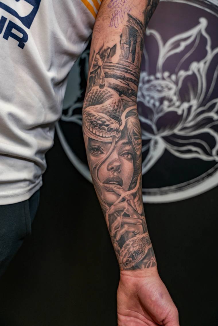 Black and grey forearm sleeve tattoo featuring a woman's portrait intertwined with a serpent, a Japanese temple above and a r