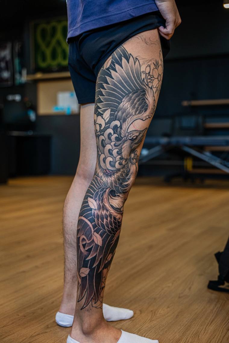 Finished irezumi greywash leg sleeve featuring a phoenix, chrysanthemum blooms, and stylized waves from thigh to ankle.